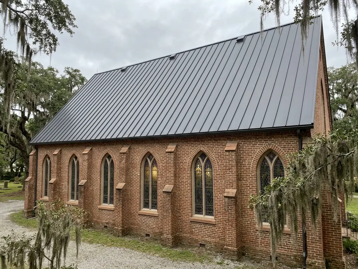 Steep dark grey standing seam roof over the nave of a brick church, with tall arched windows below